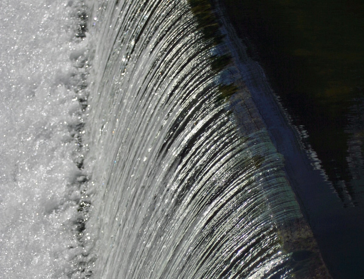 Water flowing over weir with still water to the right and turbulent water to the left.